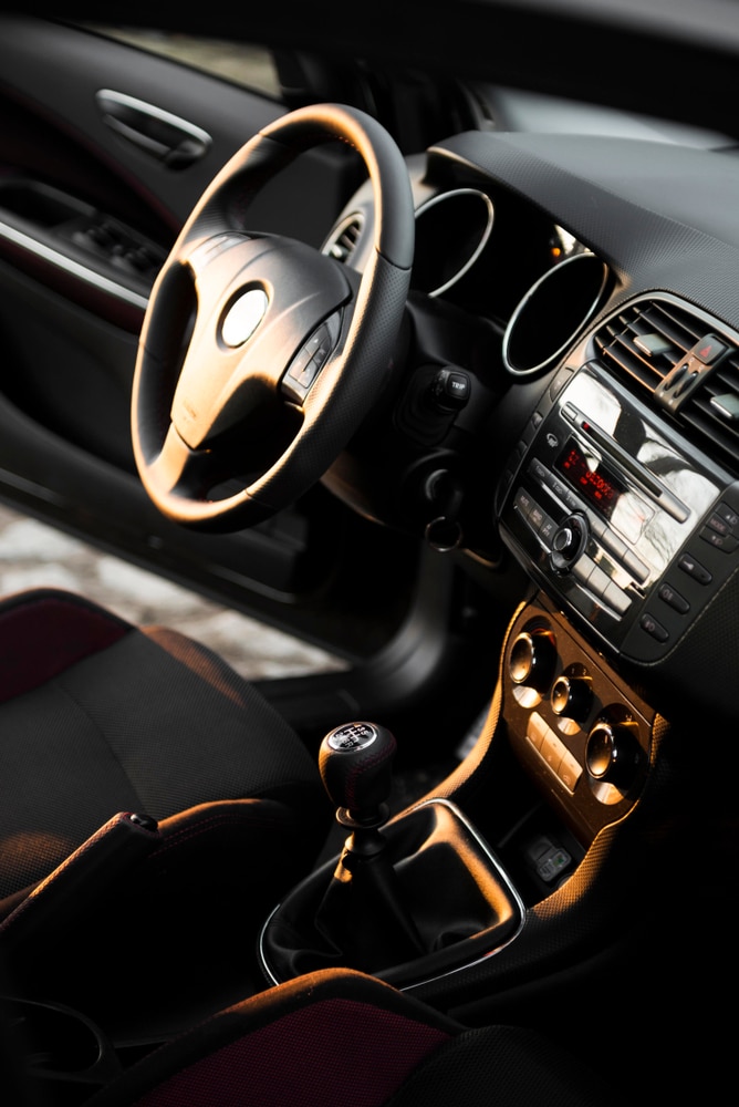 Intérieur de Voiture Sportive : Volant et Vitesse Manuelle Habitacle de voiture sportive avec volant en cuir, levier de vitesse manuel et console centrale éclairés par le soleil.