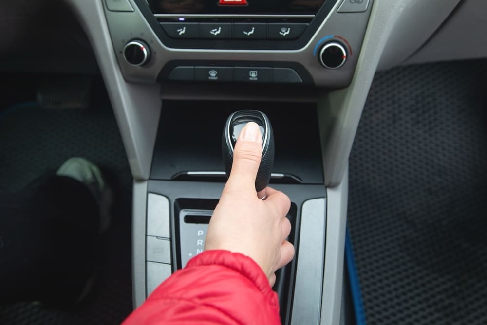 Passage de vitesse automatique : main sur le levier P R N Main en veste rouge actionnant le levier de vitesse automatique P R N d'un véhicule, console centrale visible.
