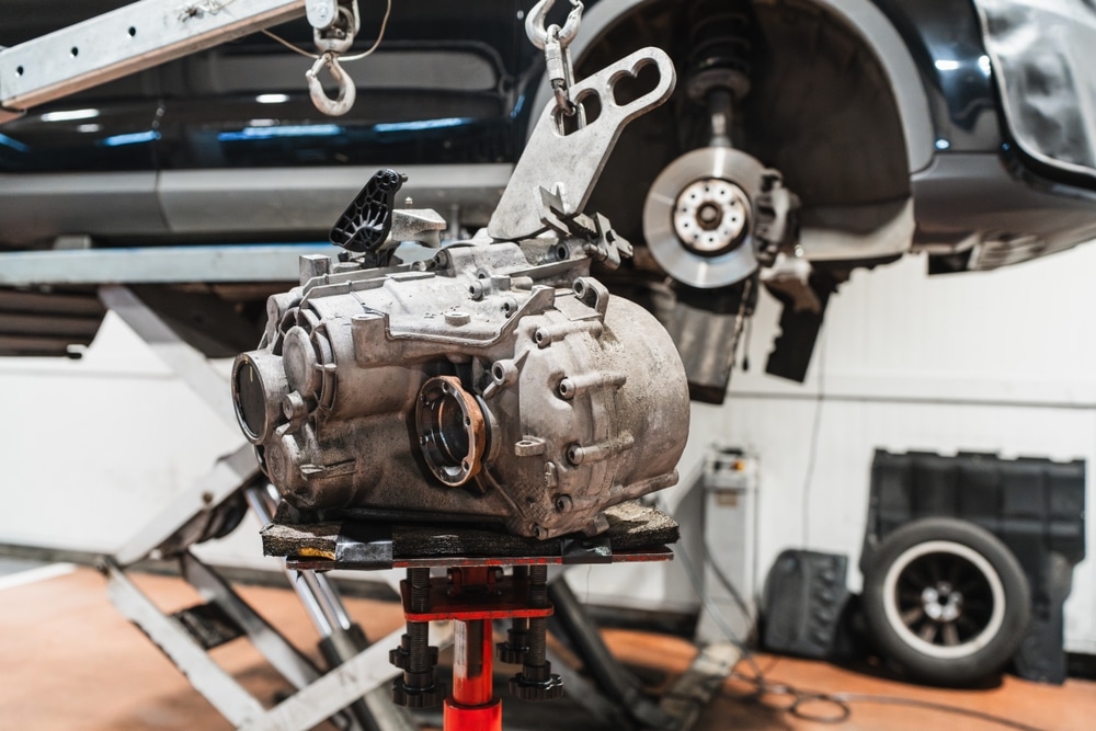 Réparation de Boîte de Vitesses et Transmission Auto Transmission de voiture déposée sur un support dans un garage avec un véhicule soulevé sur un pont élévateur mécanique.