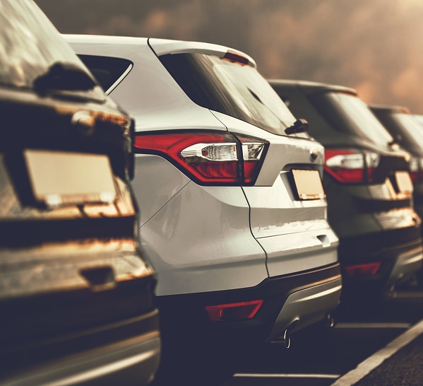 SUV d'occasion en stock : Large sélection de voitures SUV argenté stationné dans un parking extérieur au coucher du soleil avec vue arrière de plusieurs voitures.